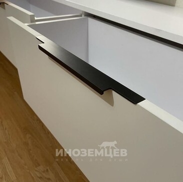 Черная накладная ручка крупным планом на белом фасаде тумбы под телевизор