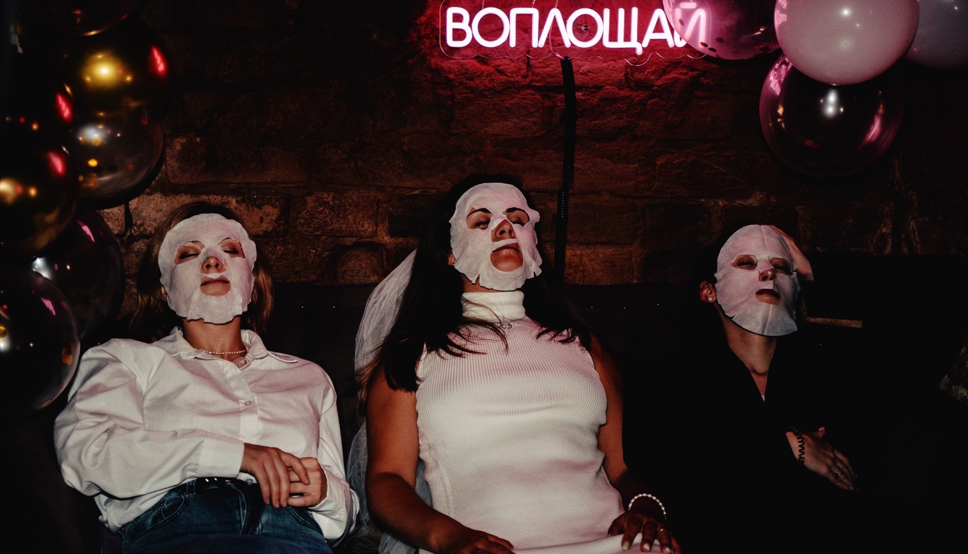 Девушки с тканевыми масками отдыхают на тематическом девичнике дома в неоновом лофте