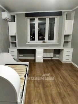 Длинный белый письменный стол под окном в детской комнате с двумя тумбами