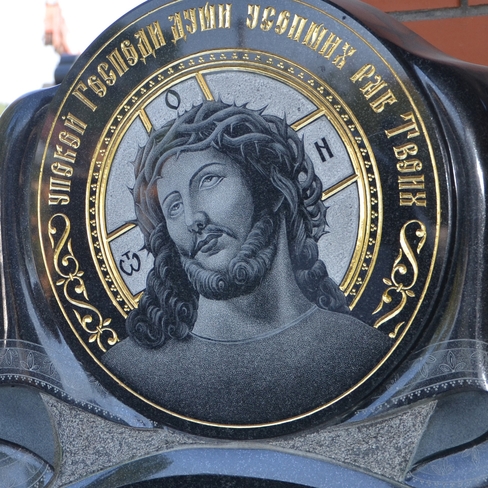 Черный гранитный памятник с выгравированным портретом Иисуса в терновом венце и золотыми надписями.