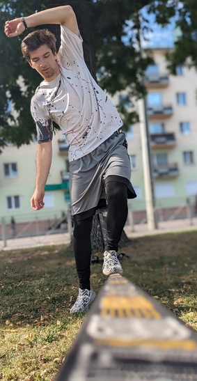 Человек тренируется на слэклайне в городском парке, сохраняя равновесие на натянутой ленте.