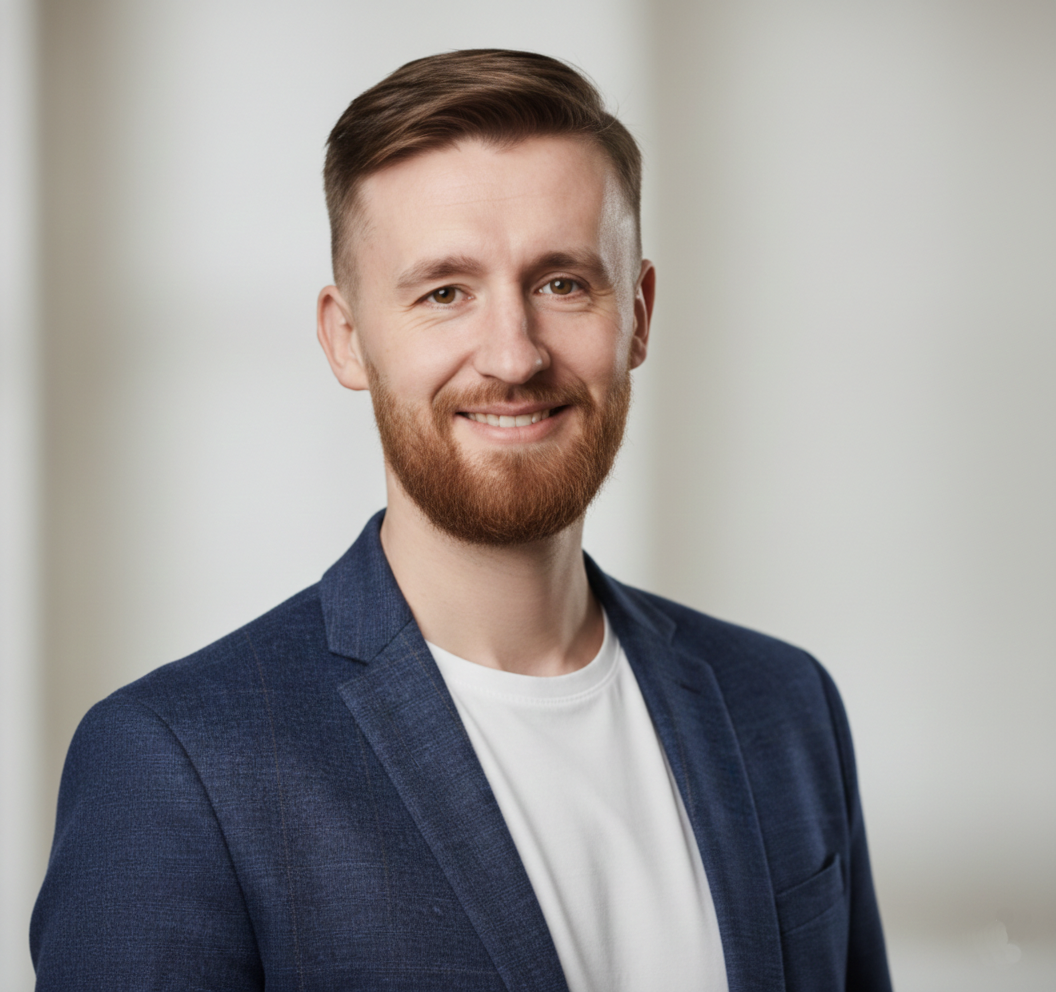 Портрет улыбающегося мужчины-психолога с бородой в темно-синем пиджаке поверх белой футболки на свет