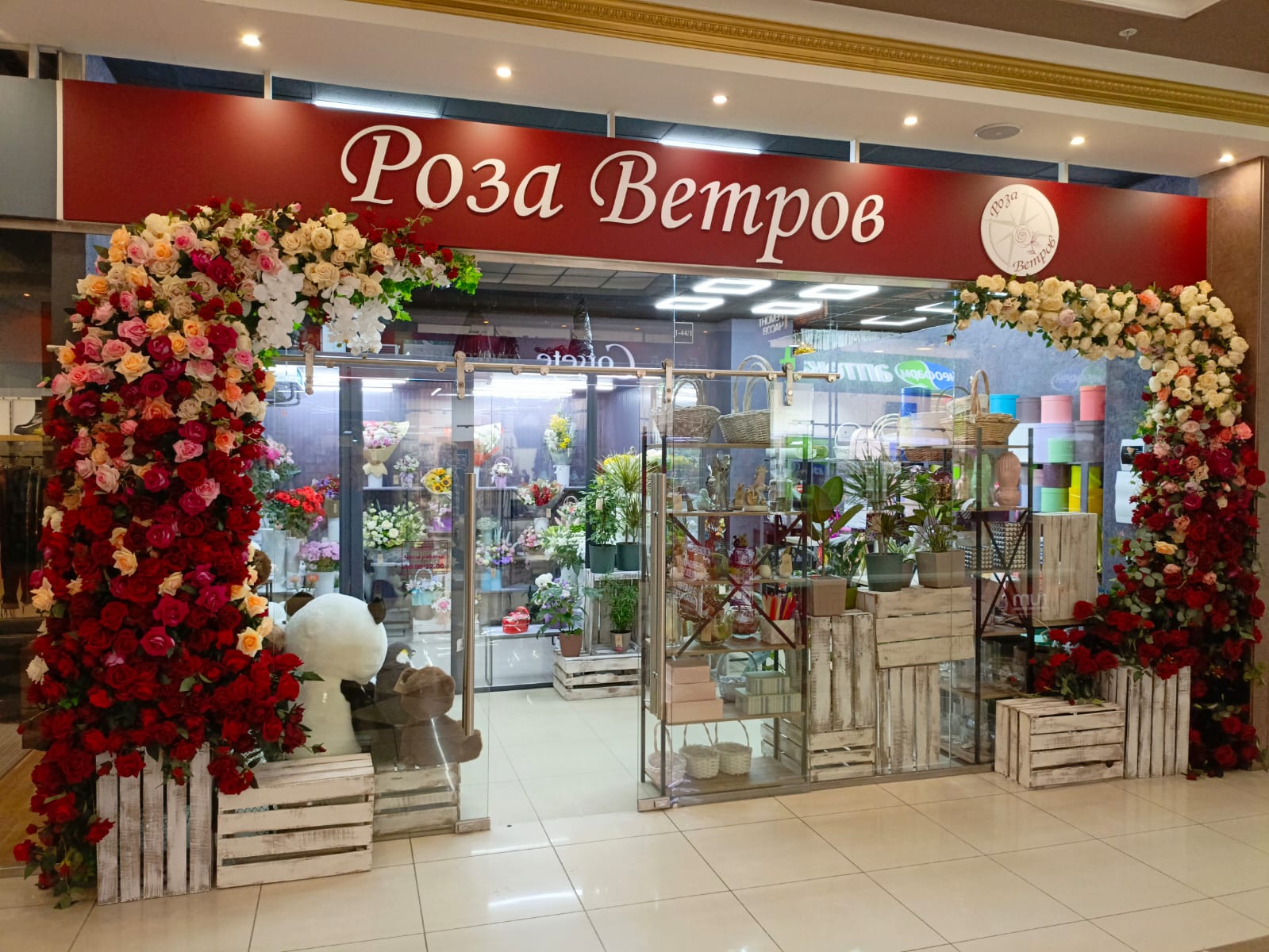 Вход магазина «Роза Ветров» в архивном кадре: две цветочные арки по сторонам двери