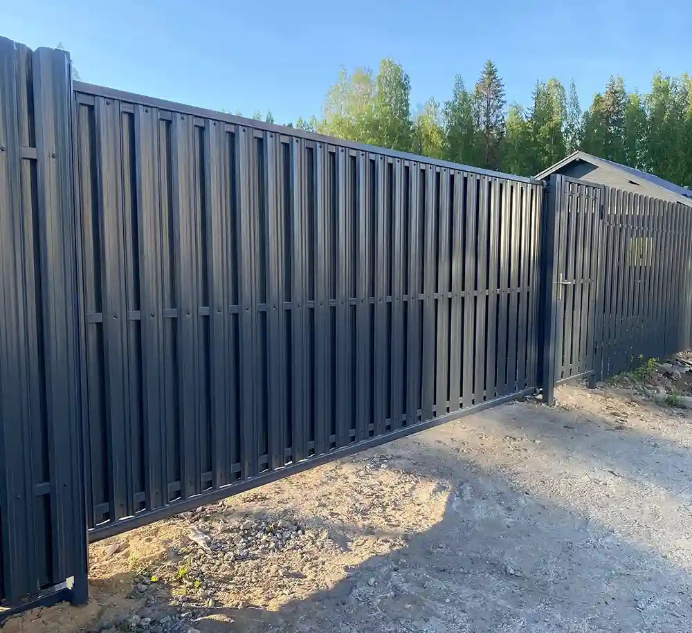 Установлен забор с откатными воротами и серым штакетником 