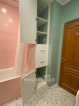 Закрытый высокий шкаф-пенал белого цвета в ванной комнате между ванной и дверью