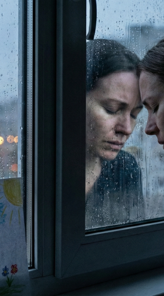 Женщина в отчаянии прислонилась к окну, рядом детский рисунок семьи — метафора боли матери в абьюзив